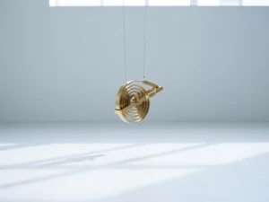 Brass spring mechanism suspended in equilibrium with coils catching natural light, casting geometric shadows on white background