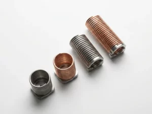 Four precision-engineered spring coils in ascending heights arranged on white surface, representing development phases in steel gray and copper tones.