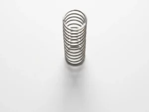 Polished steel spring suspended vertically above white surface, creating geometric coil patterns and soft shadow in minimalist composition